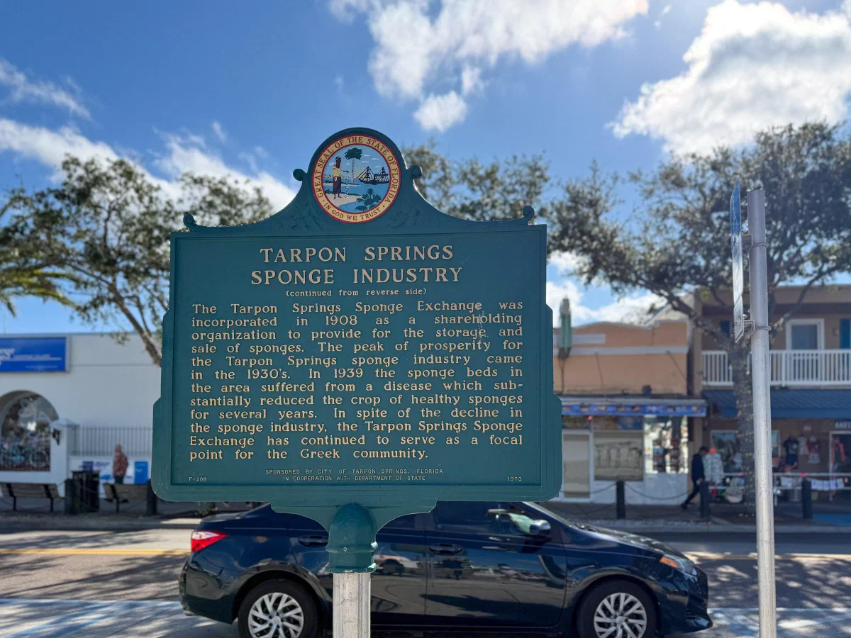 A historic marker about the Tarpon Springs sponge industry beside a street.