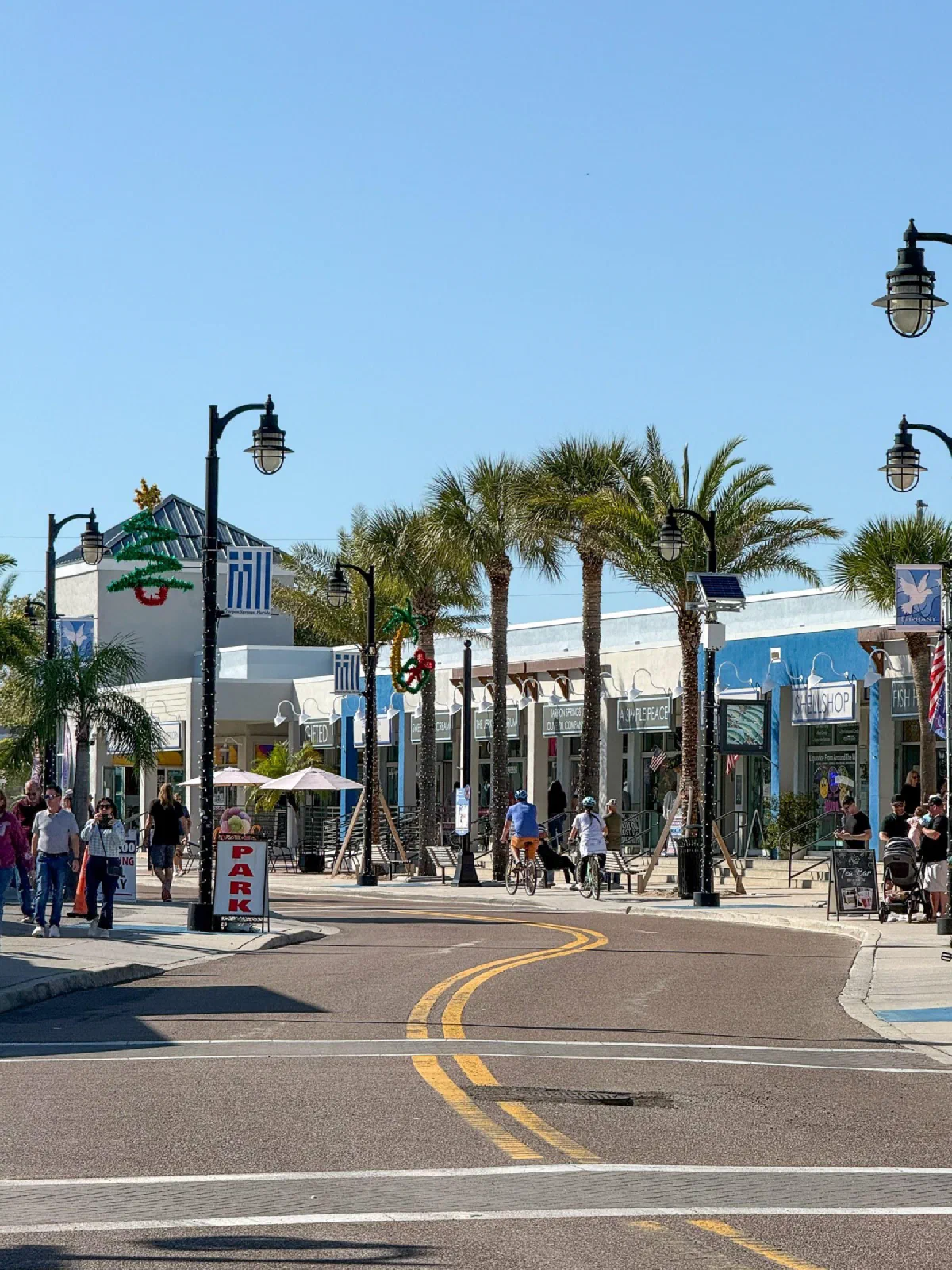 A sunny street with palm trees, decorative lamp posts, and low storefronts.