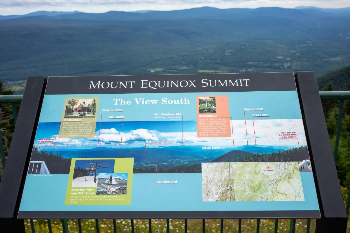 An interpretive sign labeled Mount Equinox Summit in front of a distant mountain view.