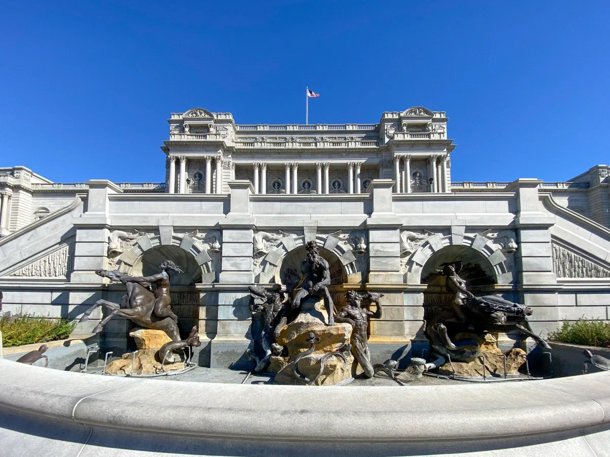 Sculpted figures in a fountain in front of a white stone building.