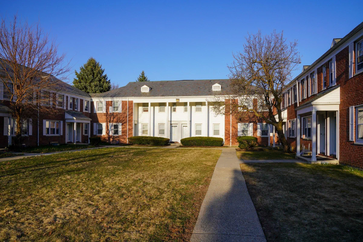 A green courtyard and a straight path between brick residential buildings beneath a clear sky.