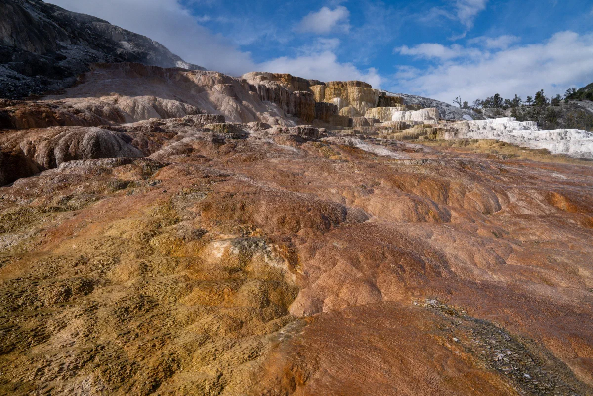 Layered pale mineral terraces and rust-colored ground beneath a partly cloudy sky.
